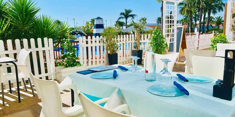 Table set with water bottles and glasses, overlooking pool area with palm trees and white fence at Lo Monte