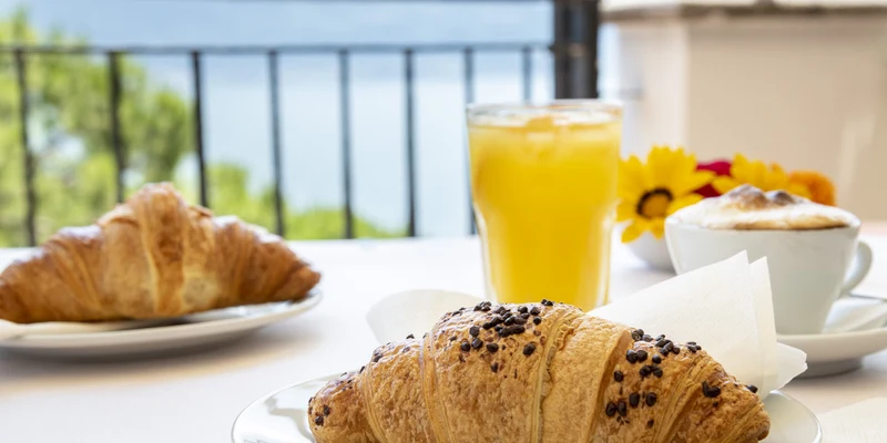Croissant and orange juice beside a cappuccino on a table overlooking a scenic outdoor view at Garda