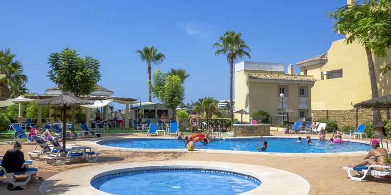 People swimming and lounging around connected pools with parasols, lounge chairs, and palm trees at Colina del Paraiso