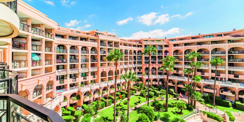 Multistory hotel surrounds lush, landscaped courtyard with tall palm trees and sunbeds, under a sunny sky at Cannes Verrerie