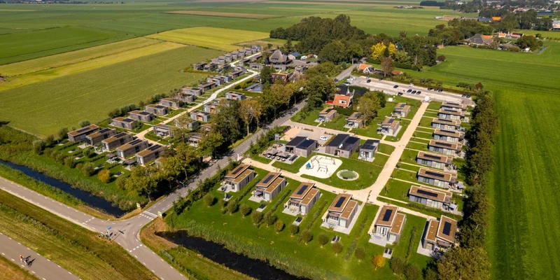 Aerial view of a campsite with cabin rows, intersecting roads, green fields, and scattered trees at Park Wijdenes