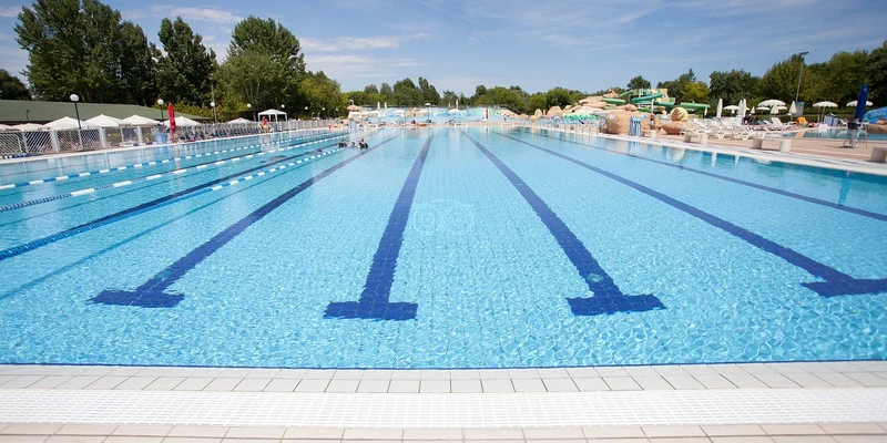 Swimming pool with clear water and lane markings, surrounded by trees and umbrellas at Marina di Venezia
