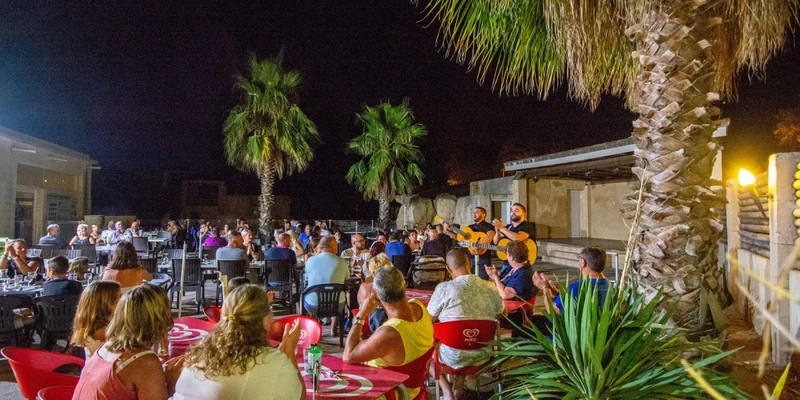 Musicians playing guitars entertain seated audience outdoors at night in a tropical setting at La Prairie 