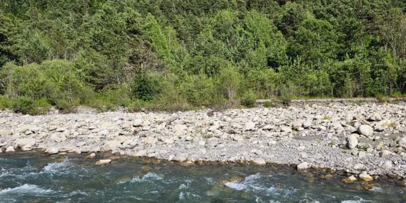 River flowing over rocks, near a rocky shoreline, with lush forest and a mountain in the background at Paradis Les Relarguiers