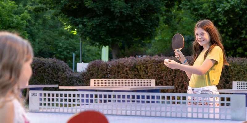 Two girls are playing table tennis outdoors, surrounded by greenery at Les Mathes