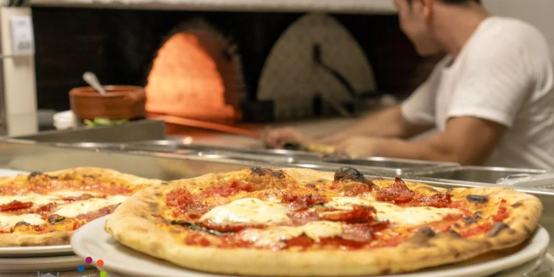 Pizza on plates; being cooked in a brick oven; man working next to it at Spiaggia Lunga