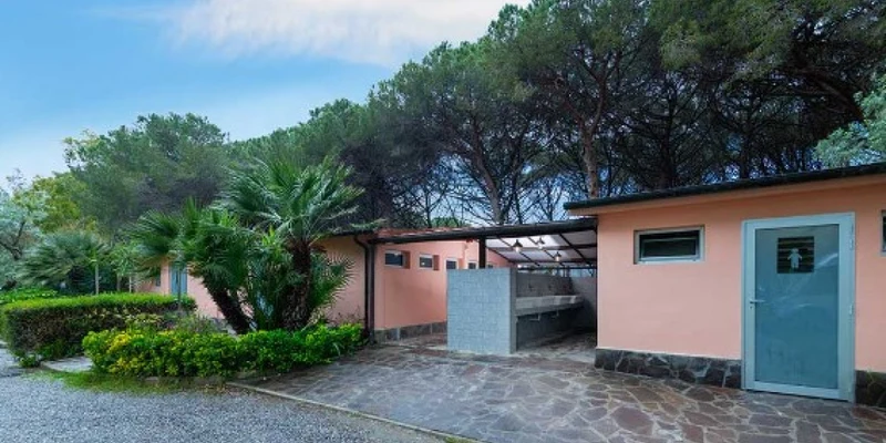 Orange-painted restroom building with tiled pathway amidst greenery and trees at Molino a Fuoco