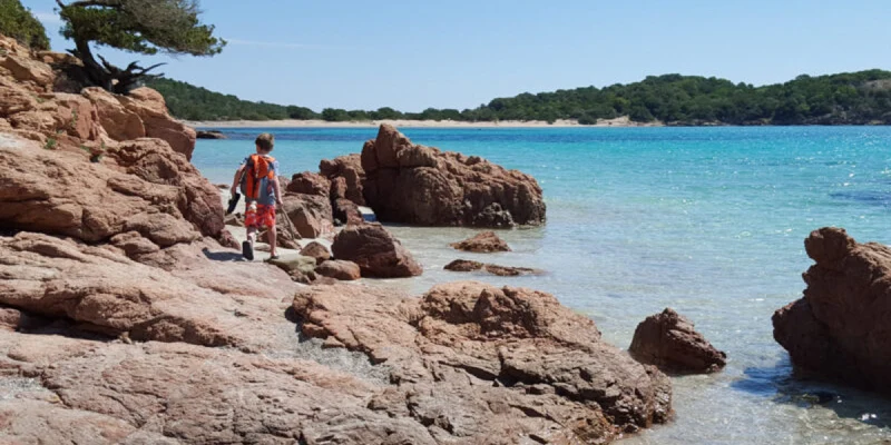 Child explores rocky shoreline by a pristine, turquoise sea with a distant forested horizon at Bella Vista