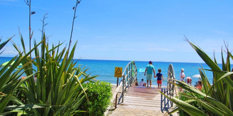 Family walking on a pathway surrounded by greenery towards a sandy beach and blue ocean at Residence Sognu di Rena