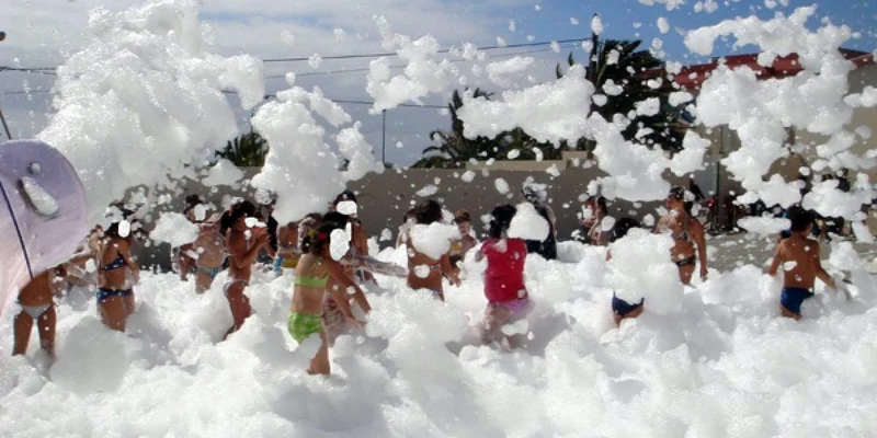 Children play surrounded by foam in an outdoor area with trees and buildings at Lo Monte