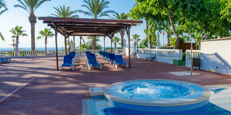Jacuzzi bubbling, sun-loungers arranged under pergola, surrounded by palm trees and overlooking sea - at Playa Tropicana