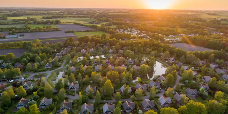 Aerial view of numerous cabins nestled in a lush, green landscape at sunset, surrounded by fields and trees at Villapark de Weerribben
