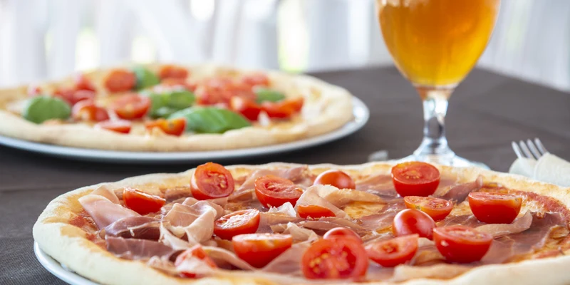 Pizzas with cherry tomatoes and basil lie on plates next to a glass of beer on a table at Fontanelle