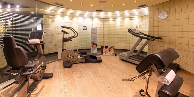 Exercise equipment, including a treadmill and stationary bike, in a well-lit fitness room with wooden flooring and mirrors at Cristal Palace Resort