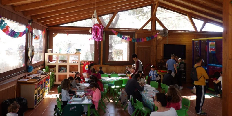 Children doing crafts and activities, supervised by adults, in a decorated wooden cabin with large windows at Cabopino