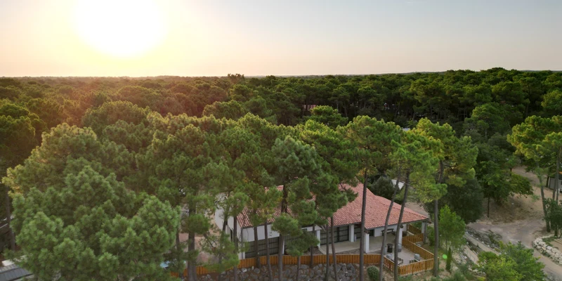 A house with a red roof nestled among tall trees during sunset, surrounded by a dense forest at Domaine de Montcalm