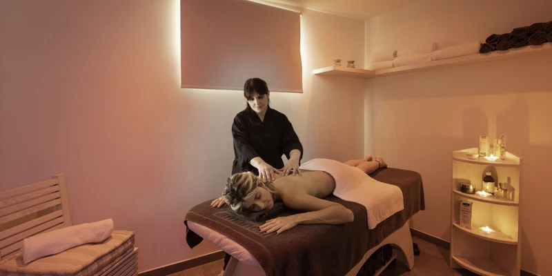 A massage therapist massages client's back on table in a dimly-lit spa room at Riva di Ugento