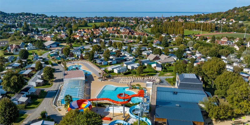 Aerial view of a vibrant water park featuring colorful slides, surrounded by lush greenery and houses at Marvilla Parks La Vallée