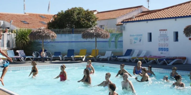 People participate in a poolside exercise class, led by an instructor, at a resort with loungers and buildings nearby at Caravanile