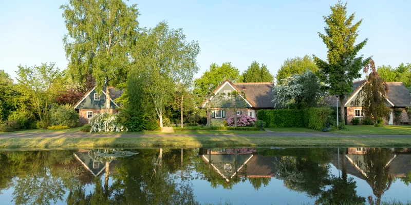 Houses reflected in a pond, surrounded by lush greenery and flowering bushes at Villapark de Weerribben