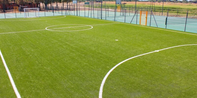A soccer field sits empty, adjacent to tennis courts, with trees and an open landscape in the background at Club Degli Amici