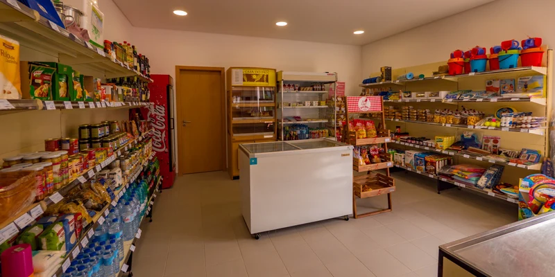 A small store displaying various groceries and supplies on shelves, with a freezer unit in the center at Valado