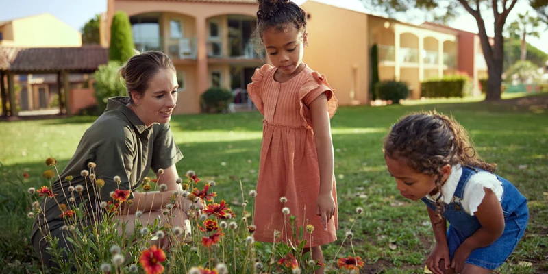 Three people examining flowers in a grassy area with buildings in the background at Les Rives de Cannes Mandelieu