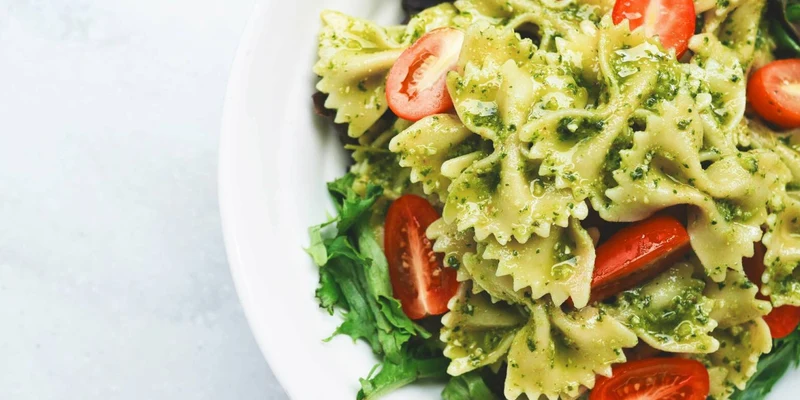 Bowl of pasta with pesto sauce and cherry tomatoes served on leafy greens at Villenpark Sanghen
