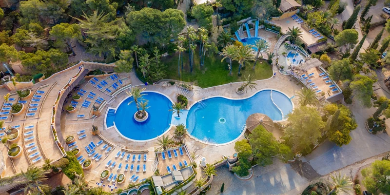Swimming pool surrounded by sun loungers and palm trees, nestled within a lush forest setting at Playa Bara
