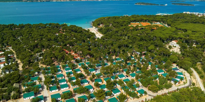 Rows of cabins with green roofs nestled among trees along a picturesque coastline at Park Soline