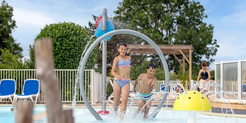 Children playing in a splash pad with water features, surrounded by lounging chairs and greenery at Mont Saint Michel