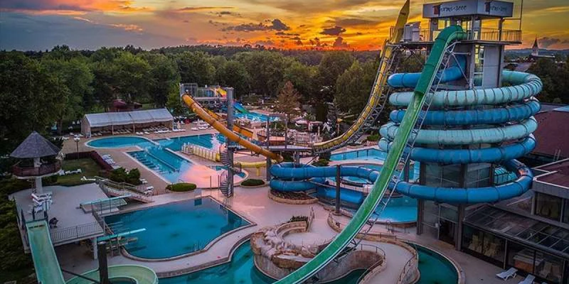 Waterslides twisting above pools in an amusement park during sunset, surrounded by trees and recreational facilities at Terme 3000