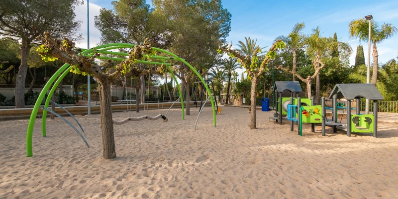 Playground with slides and swings under palm trees, situated in a sandy area at Playa Bara