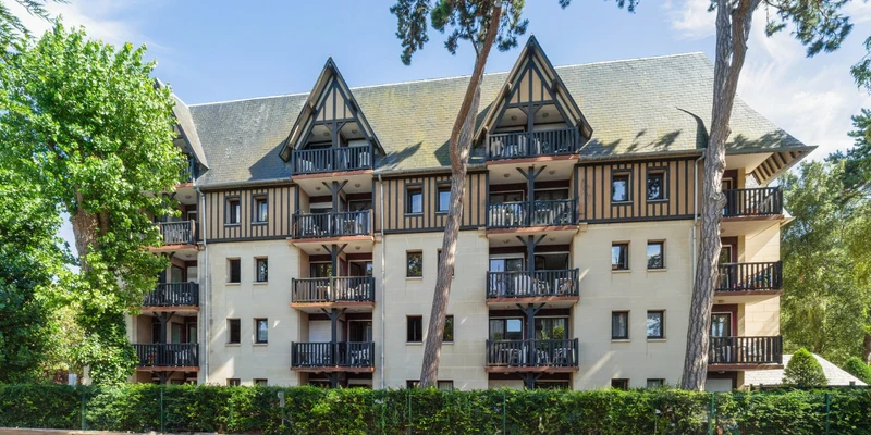 Four-story building with wooden balconies and slanted roofs, surrounded by trees and greenery at Residence Les Embruns
