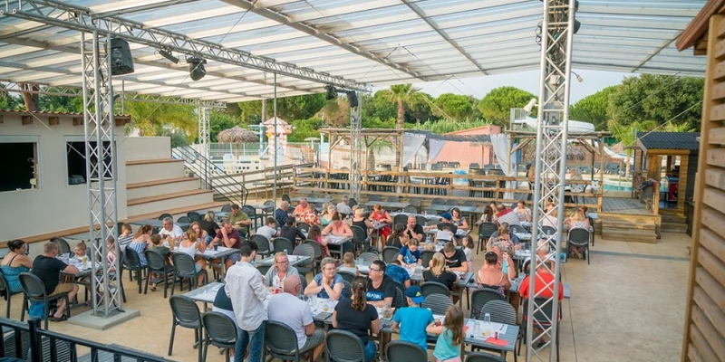 People dining at tables in an outdoor covered area with greenery and a pool in the background at Paradis le Pearl