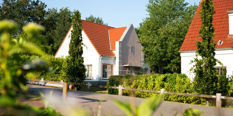 White house with red roof surrounded by greenery and trees, under a clear blue sky at Ferienresort Bad Bentheim