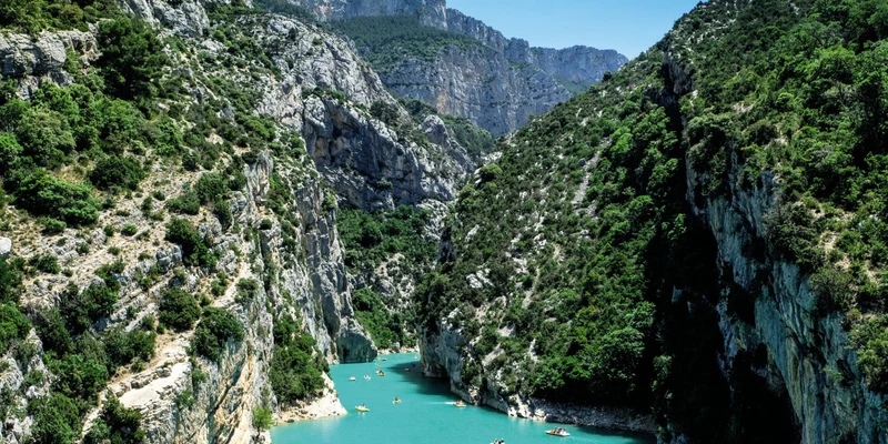 Kayakers paddling on a turquoise river, surrounded by steep, rocky cliffs covered in lush greenery at Marvilla Parks Verdon Parc