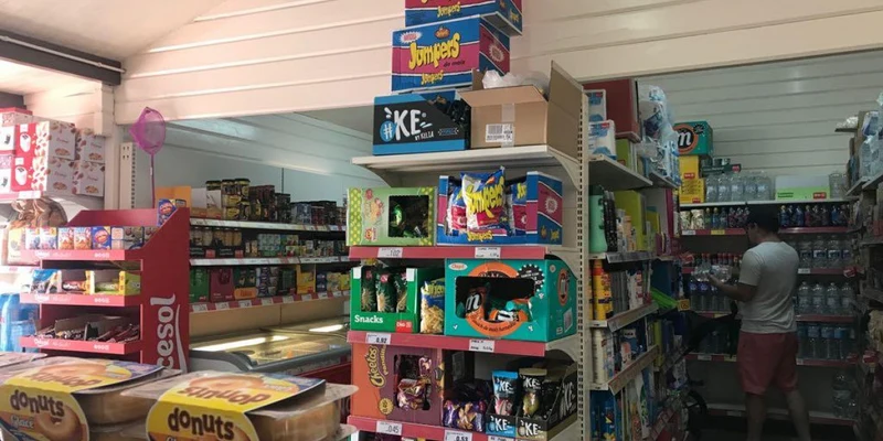 Man choosing items in grocery aisle filled with colorful snacks and various products; indoor store setting with shelves at Lo Monte