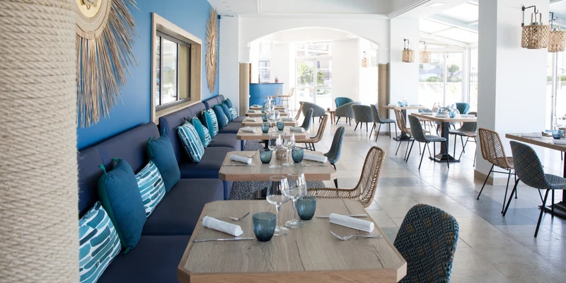 Tables and chairs are organized in a modern, airy restaurant, with blue and neutral decor at Les Bulles de Mer