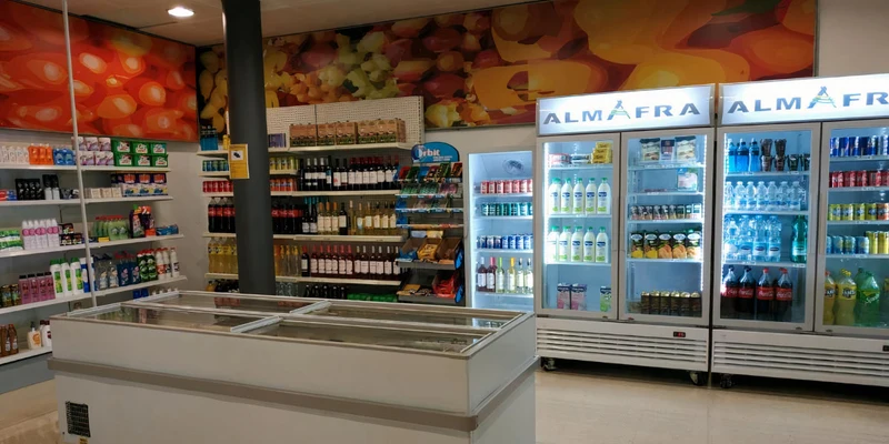 Shelves and refrigerators display drinks, food, and household items, located in a well-lit, organized supermarket section at Almafra