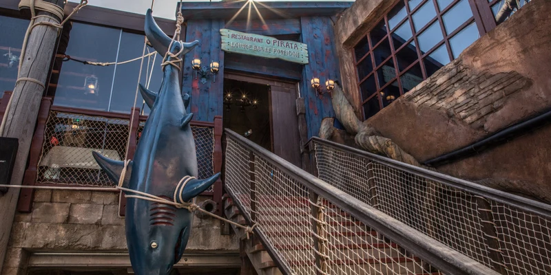 A fake shark suspended upside down outside the entrance of a rustic, pirate-themed restaurant at Resort Cap Pirate