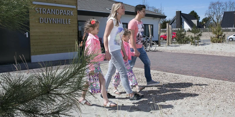 Family of four walking on sandy path past a building with beach houses in the background at Strandpark Duynhille