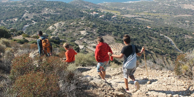 Hikers, descending a rocky path, overlook a vast coastline and green hills at Bella Vista