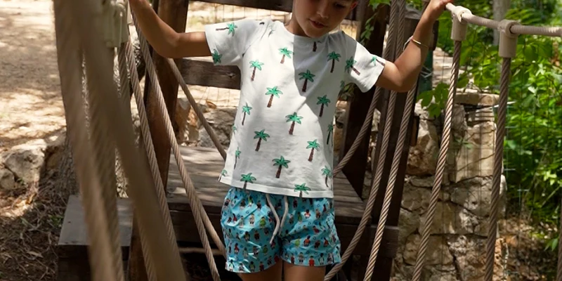 A child carefully crosses a rope bridge outdoors, surrounded by greenery and rustic wooden structures at La Scogliera