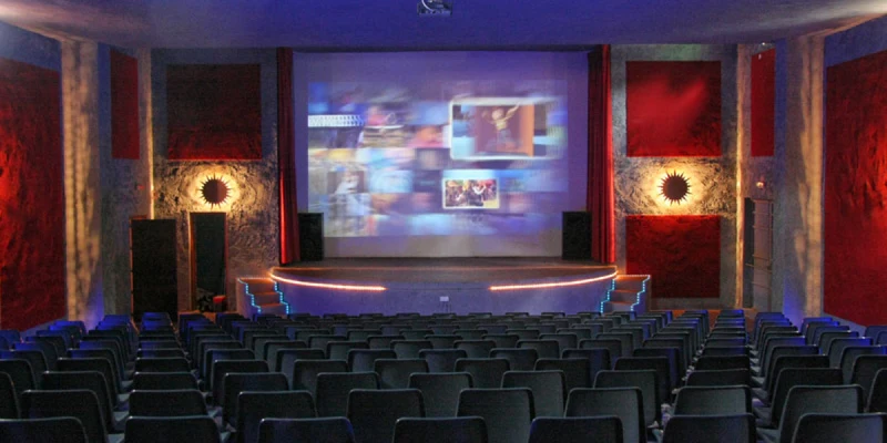 Rows of empty seats facing a large, illuminated movie screen in a dimly lit theater at El Templo del Sol