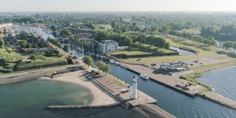 Lighthouse towering near a marina entrance as boats dock along serene canals in a coastal town at Europarcs Poort van Zeeland