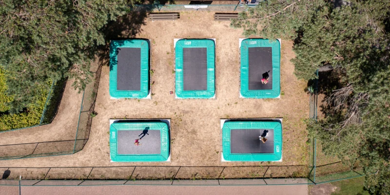 Trampolines in an outdoor facility with people jumping, surrounded by trees and a walkway at Recreatie- en Natuurpark Keiheuvel